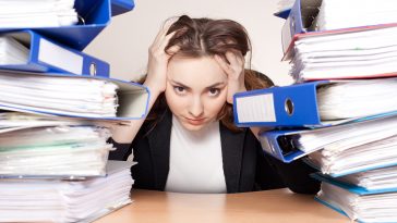 Frustrated Businesswoman With Stack Of Folders